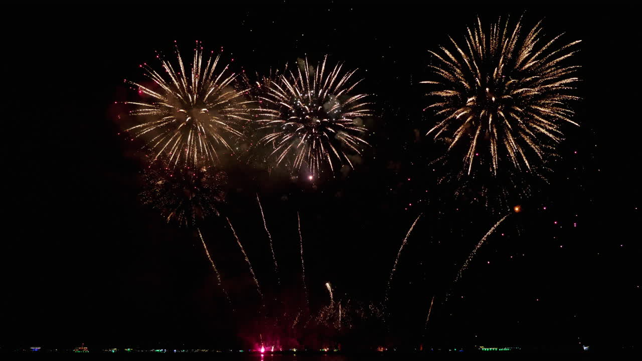 cohetes simultáneos cruzándose en diferentes colores cálidos, explosiones superiores hechas estrellas en forma de flor y en la parte inferior son rojas luego naranja y además chispas verdes, exhibición de fuegos artificiales
