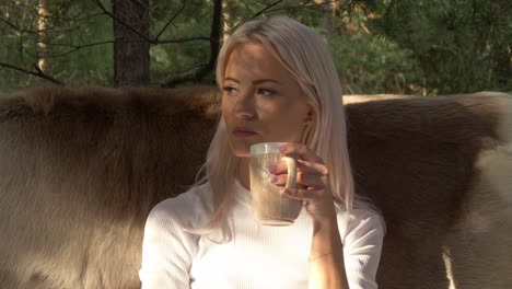 caucasian lady sitting on the rustic fur sofa having a hot drink during sunny winter morning at norwegian village in arendel, zagorow poland