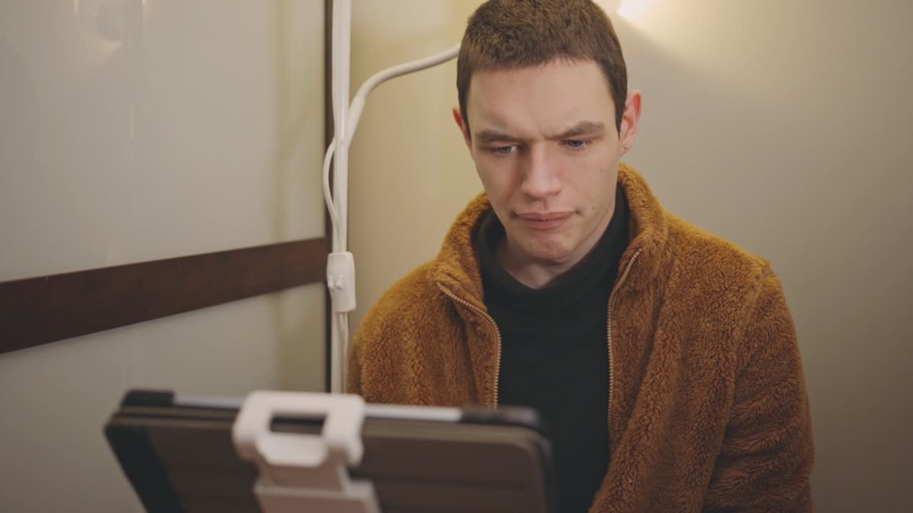 Young Man Using Video Chat On Tablet In A Room - medium shot
