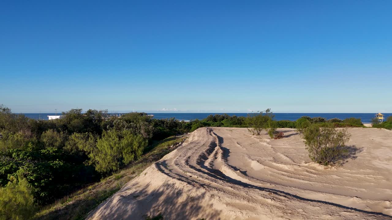 Drone footage captures expansive sand dunes and lush vegetation under clear blue skies along the Pacific Ocean coastline