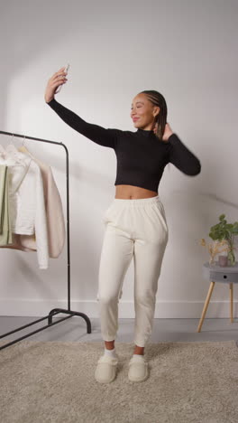 vertical pov video of female social media influencer posing for selfie producing user generated content in studio modelling a variety of fashion outfits shot in real time