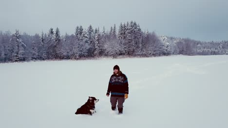 man and his alaskan malamute pet dog in deep snow - wide shot