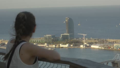 caucasian woman standing on balcony overlooking the port of barcelona with iconic hotel