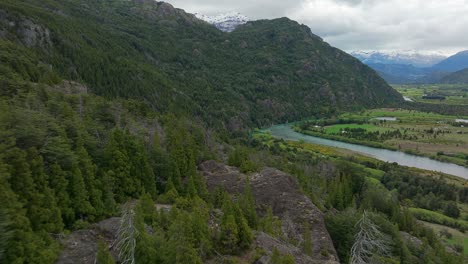 Aerial-Flying-Over-Forested-Hillside-To-Beside-Futaleufu-River-With-Snow-Capped-Mountains-In-Background