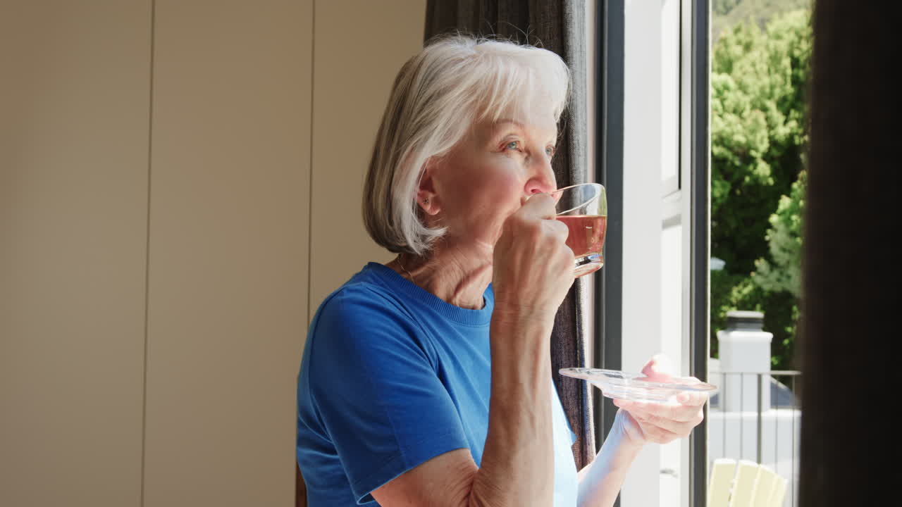 Gazing outside, senior woman sipping tea peacefully by window at home
