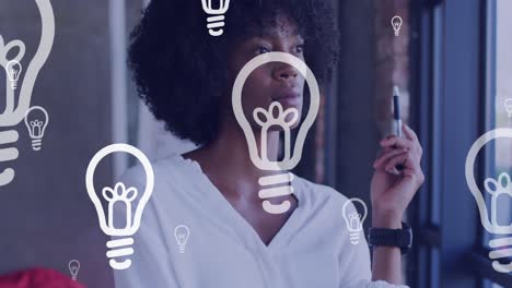 Composite-video-of-multiple-bulb-icons-floating-against-thoughtful-african-american-woman-at-office
