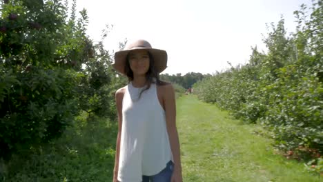 mujer caminando por un huerto se gira para mirar a la cámara.