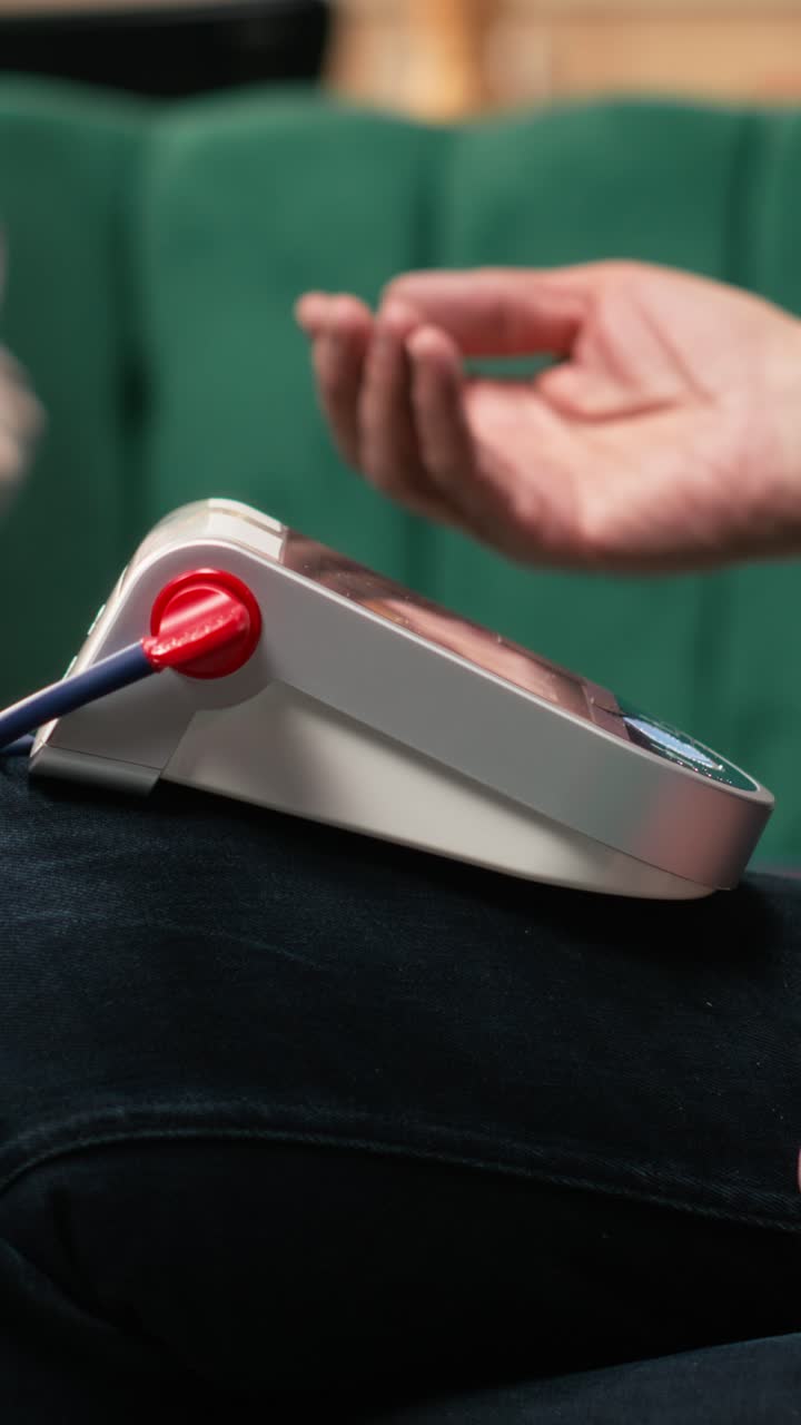 Video verticale. Uomo anziano in pensione che controlla la pressione sanguigna e il polso usando un misuratore di pressione.