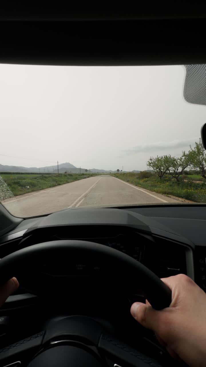 Perspetiva de condução de um carro por uma estrada rural curva através de paisagens campestres. Mãos no volante com a vista do para-brisa da estrada aberta durante uma viagem diurna