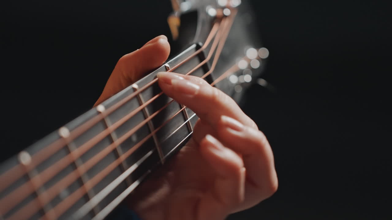 Primo piano della tastiera di una chitarra acustica che mostra il posizionamento preciso delle dita durante una tranquilla pratica fingerstyle, bagliore caldo dello studio, profondità di campo ridotta, sfondo scuro, musicista solista concentrato sulle transizioni degli accordi.