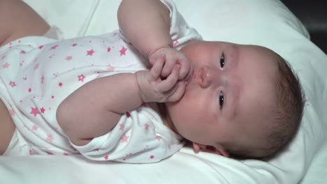 Caucasian-Little-cute-girl-lies-on-her-back-in-a-white-bodysuit-and-puts-her-fingers-in-her-mouth