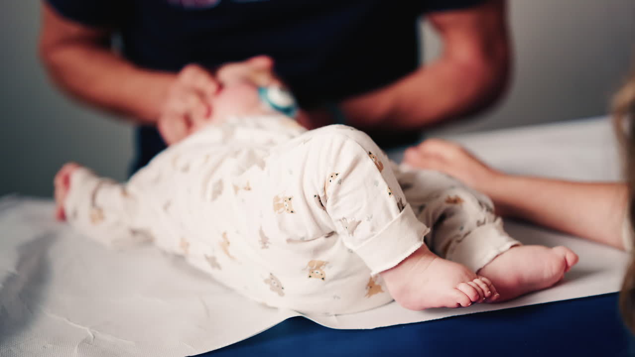 Close up of an infant's legs and feet while caregivers gently reposition the baby during a care or examination session