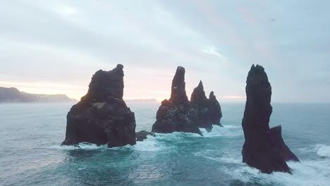 reynisdrangar rocks at reynisfjara beach next to vik i myrdal at south iceland. aerial drone shot flying over a cliff during sunrise. large storm waves crash rock. high resolution footage. 4k