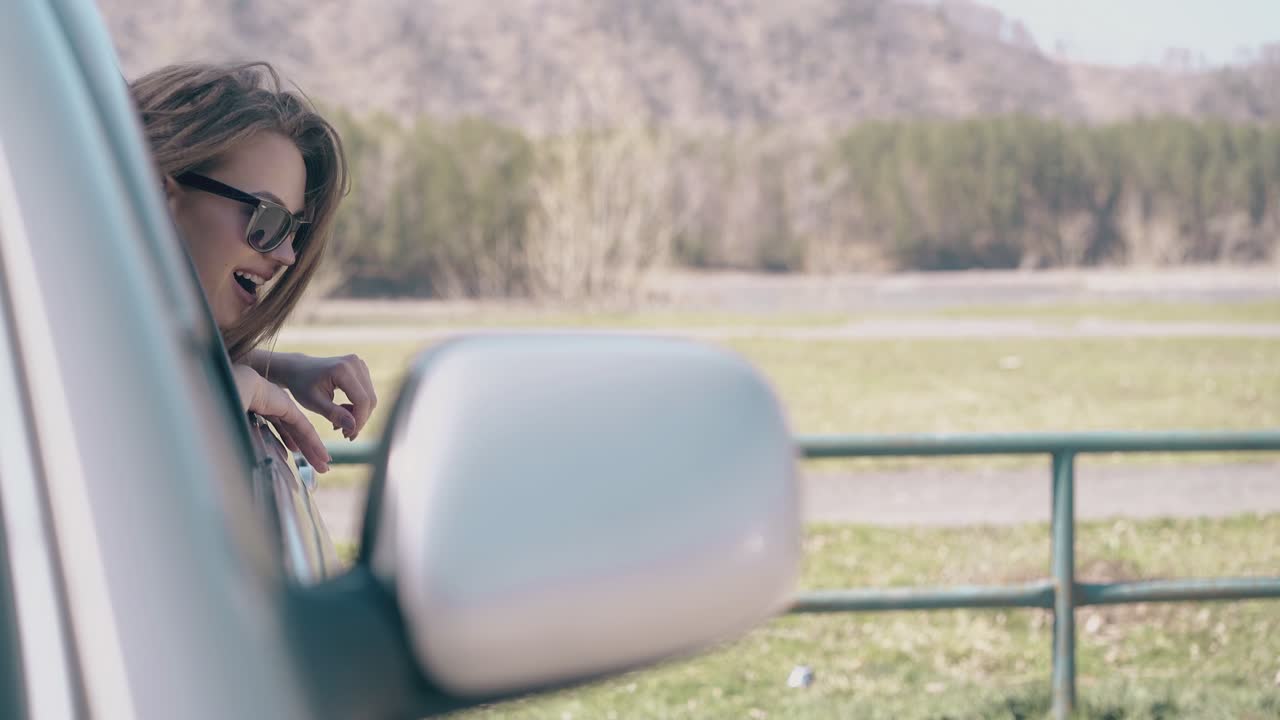 chica alegre se inclina hacia fuera de la ventana del coche en tierras de cultivo cámara lenta