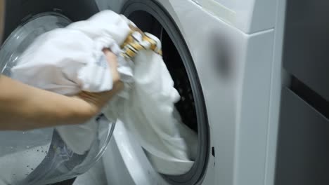 woman doing laundry with washing machine at home. female gets out white clothes of washing machine