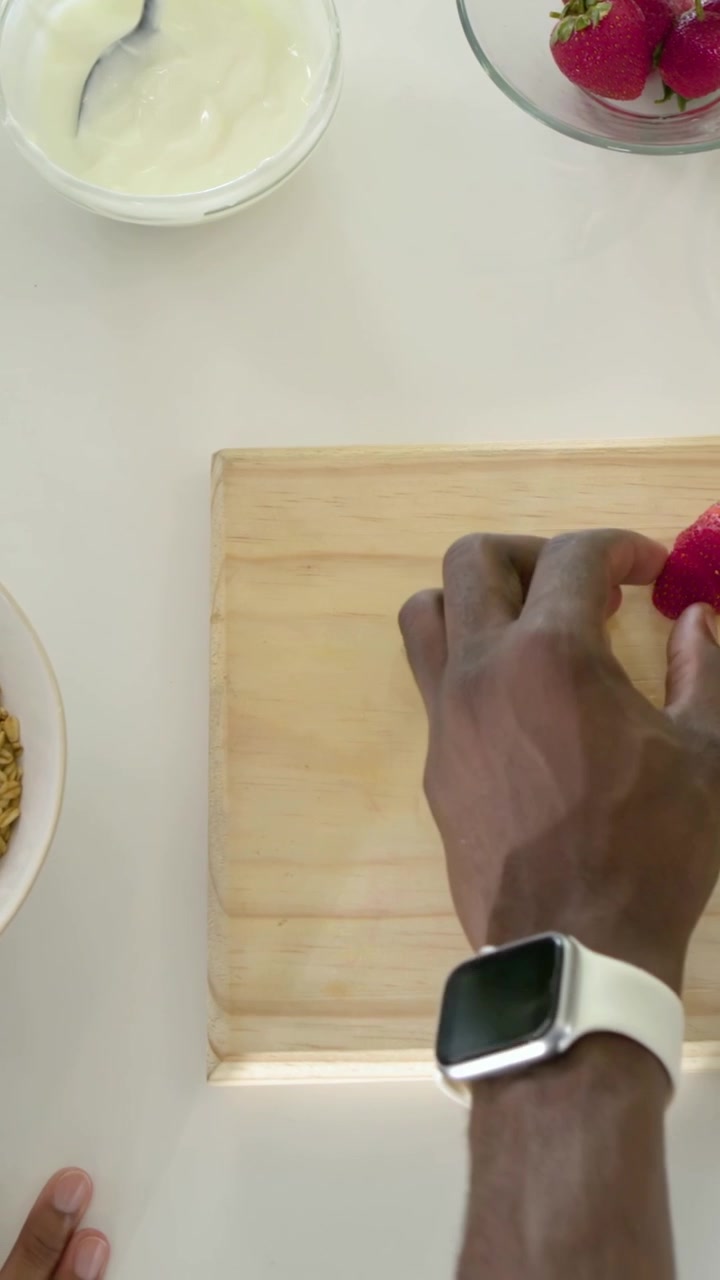 Vertical video: Right hand entering lifting berry removing top on home counter for bowl, copy space
