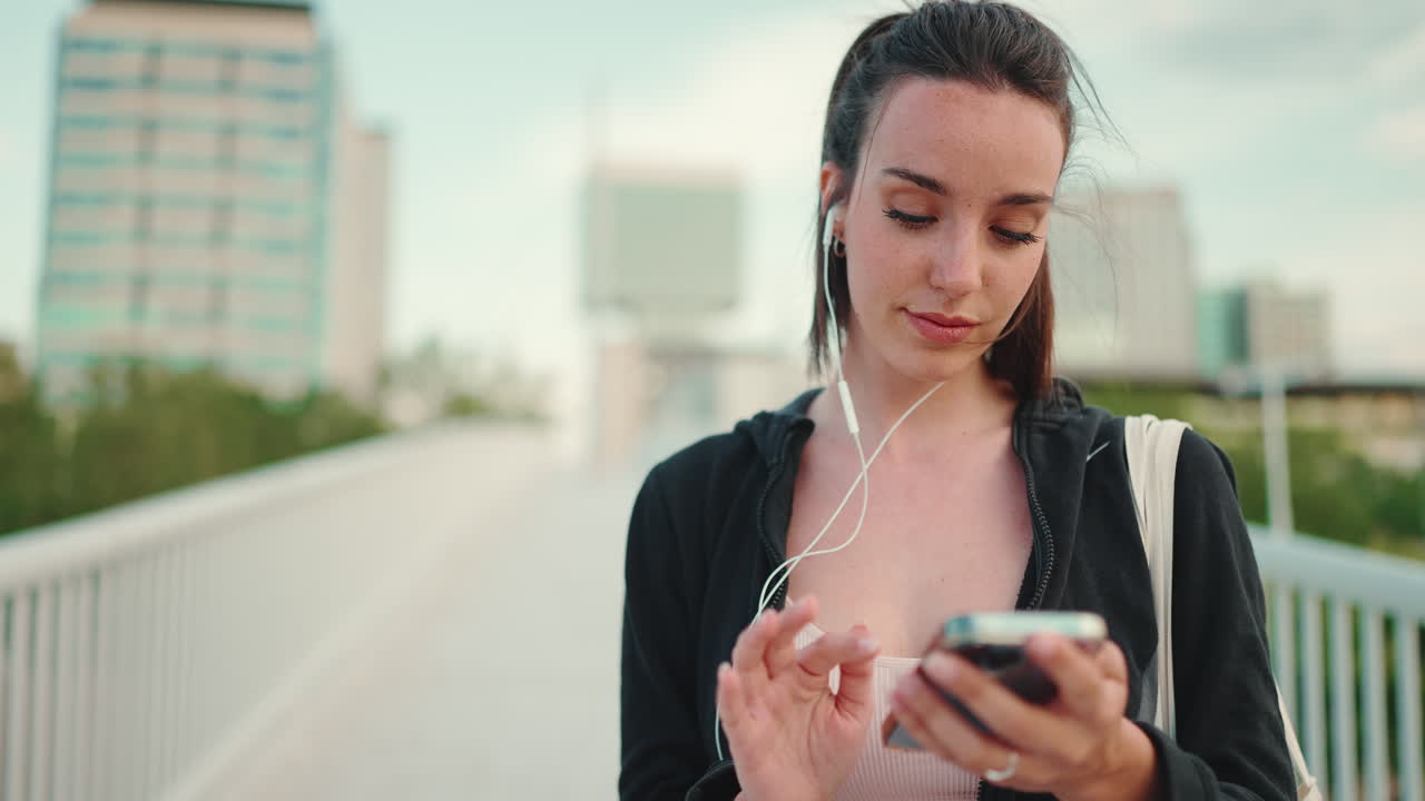 Woman using phone with headphones on a bridge