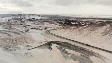 Vista-De-Seguimiento-Aéreo-Desde-Lejos-De-Los-Camiones-Que-Circulan-Por-Una-Ruta-Curva-En-Invierno,-Rodeados-De-Vastas-Tierras-Y-Montañas-Salvajes-Del-Norte-Nevadas-Blancas,-Un-Paisaje-Cinematográfico-Espectacular