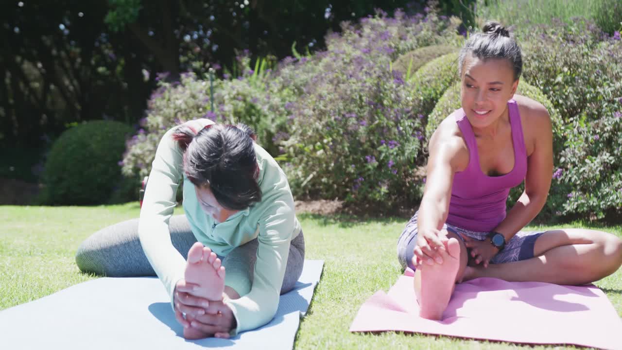 hermanas bi-raciales felices haciendo yoga y estirándose en el jardín, en cámara lenta