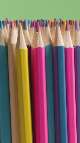 Vertical-Video-Studio-Shot-Of-Rotating-Multi-Coloured-Pencils-Against-Green-Background