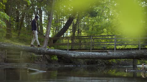 black man crossing a creek on tree trunk bridge in the woods - left to right