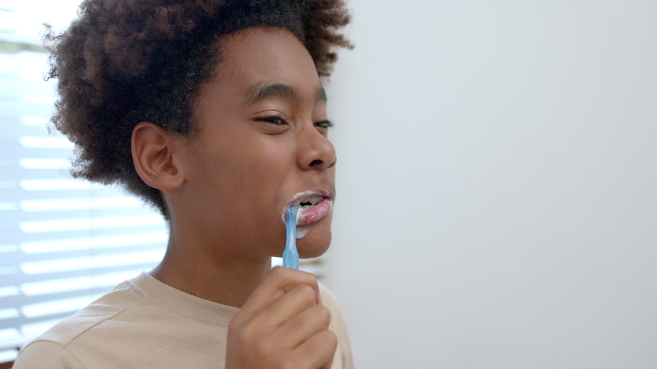 African american boy brushing teeth in bathroom, slow motion