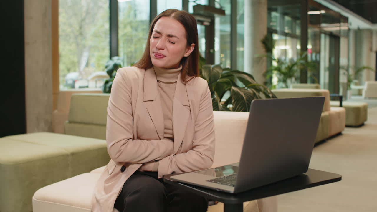 노트북을 사용하는 실망한 백인 사업가 여성이 사무실 로비에서 갑작스러운 위통을 느습니다.