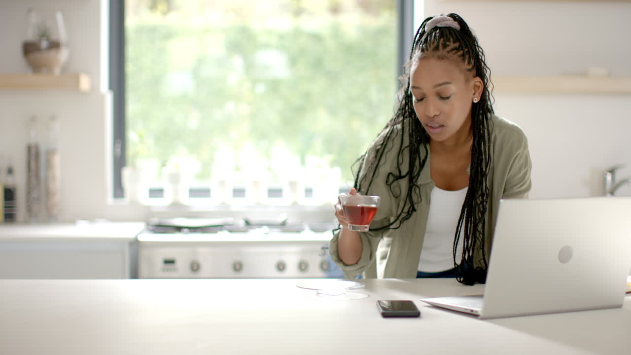 African American young woman drinking tea and using laptop