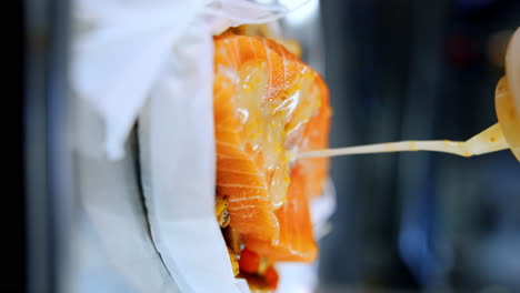 piece of salmon on the vegetable layer. a sauce is poured on the meat from a bottle. close up. vertical screen.