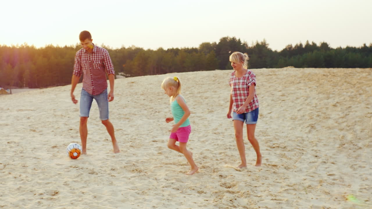 Families With A Child Playing Football In The Sand On The Beach