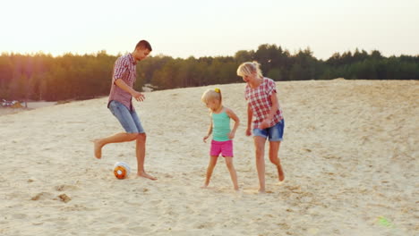 familias con un niño jugando al fútbol en la arena de la playa