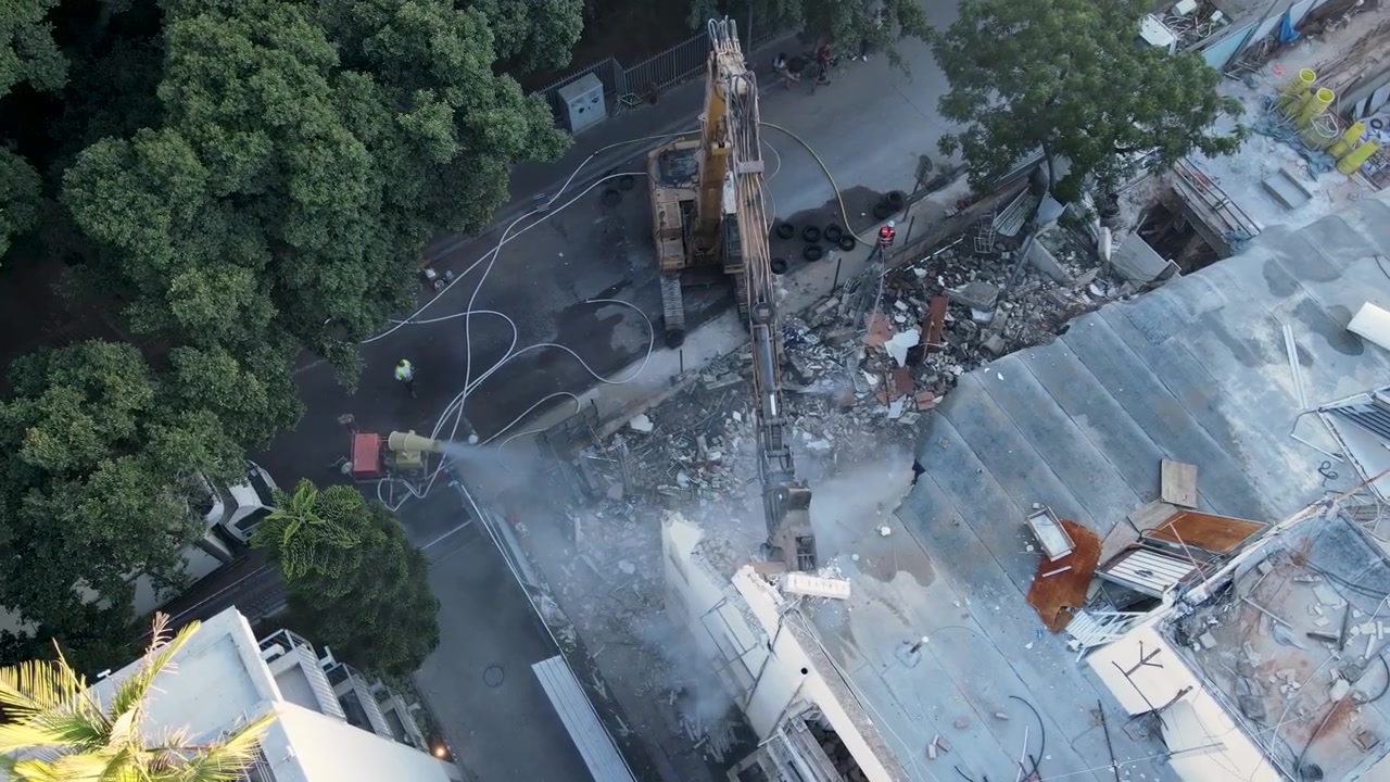Chantier de démolition avec une pelle mécanique abattant un toit pour une infrastructure de réaménagement, vue aérienne par drone