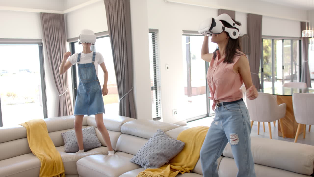 Wearing VR headsets, two teenage girls enjoying virtual reality experience at home