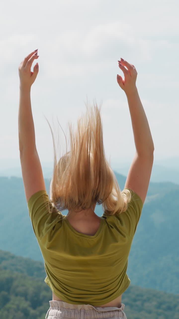mujer elegante en ropa casual levanta el cabello largo sintiendo felicidad de pie contra el pintoresco valle en las montañas silueta en verano vista trasera
