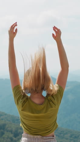 elegant woman in casual clothes lifts up long hair feeling happiness standing against picturesque valley at mountains silhouette in summer backside view