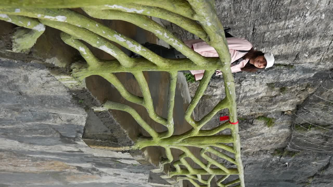 Tourist in pink jacket over a cliff enjoys her visit to Tianmen Mountain, Zhangjiajie. Vertical