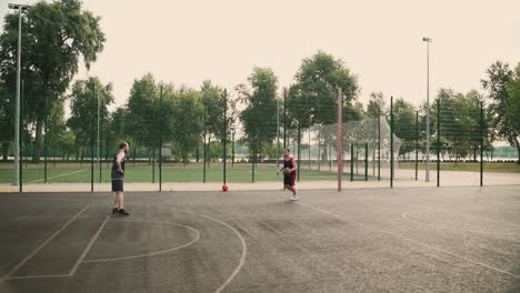 Ein-Geschickter-Basketballspieler,-Der-Den-Ball-Zwischen-Den-Beinen-Gegen-Seinen-Gegnerischen-Verteidiger-Dribbelt,-Den-Ball-In-Einen-Basketballkorb-Im-Freien-Wirft-Und-Sich-Gegenseitig-High-Five-Gibt