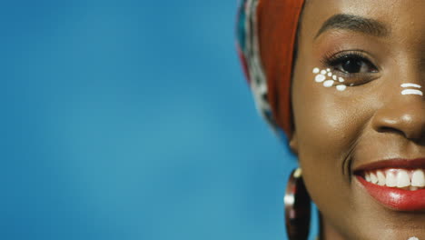 vista de cerca de la mitad de la cara de una joven afroamericana alegre con turbante y maquillaje sonriendo alegremente a la cámara