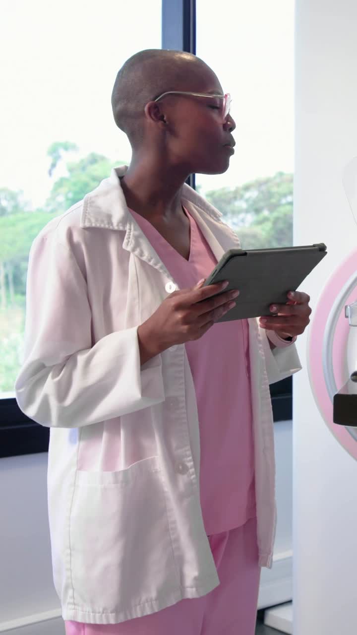 Vertical video: Checking tablet, clinician in pink scrubs gesturing at pink unit by clinic window