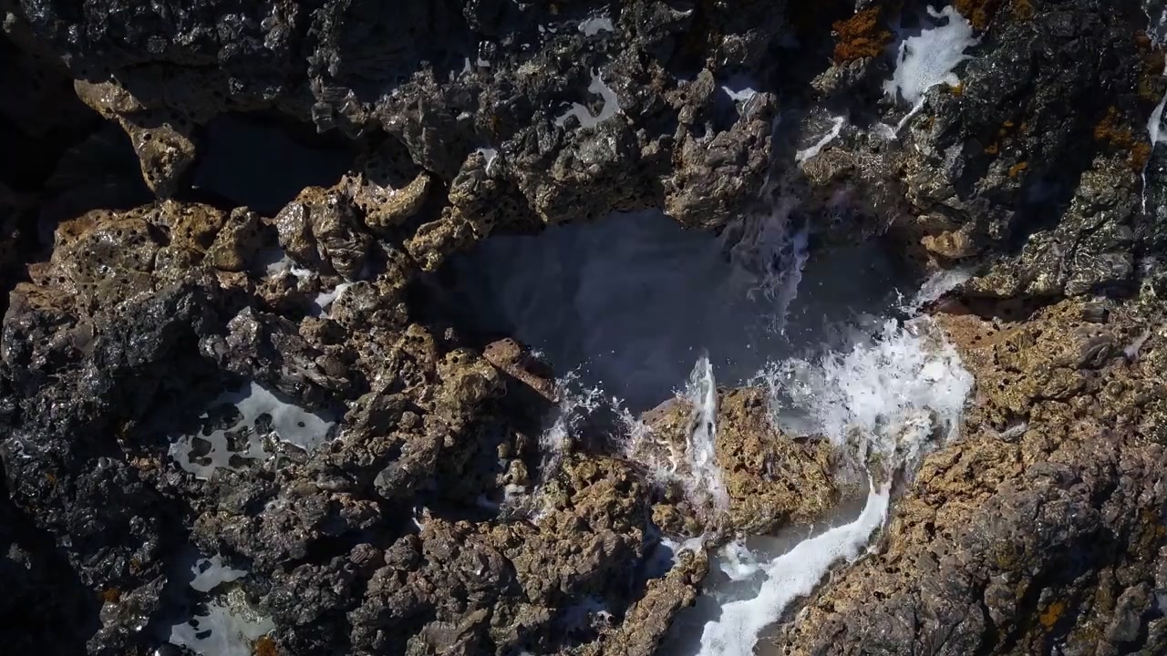Ripresa aerea statica che mostra una grotta marina con acqua dell'oceano che vi defluisce sulla costa frastagliata di Hookena Beach alle Hawaii, Big Island.