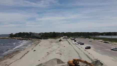 aerial drone descending jib down to reveal a earth mover digger at sandy beach in cohasset ma, reshaping the beach