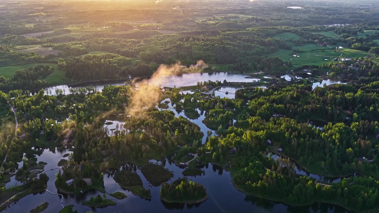 Luftfoto af lettisk sø med øer, skovområde og luksusresortbygninger ved solopgang