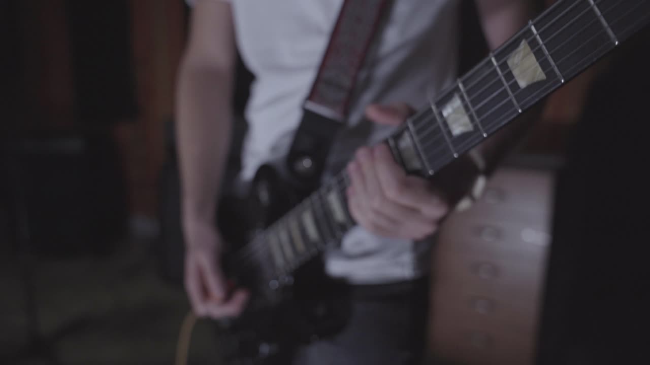 Young man practicing electric guitar in basement. Close up on hands, guitar
