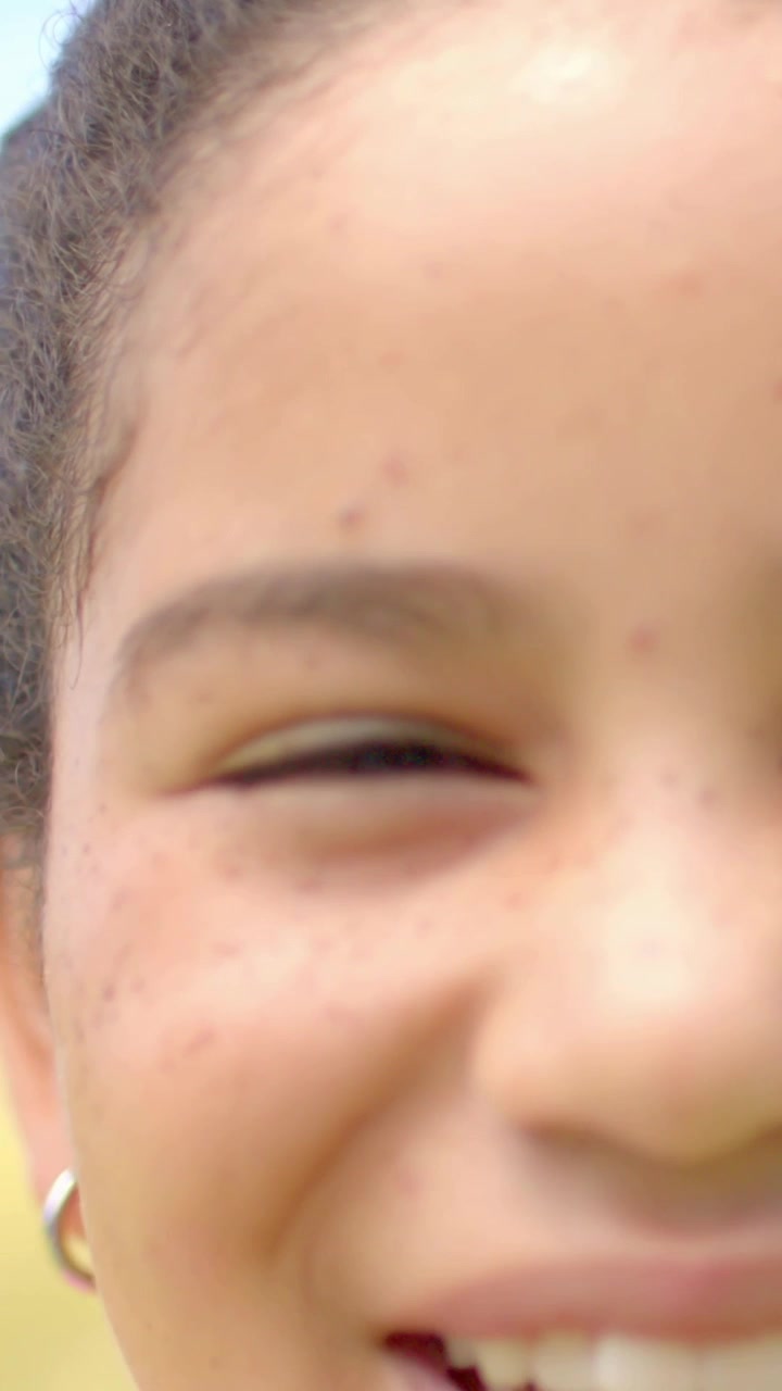 Video verticale: Adolescente sorridente che strizza gli occhi per il sole, telecamera che si allontana, campo che si sfoca, orecchino a cerchio visibile.