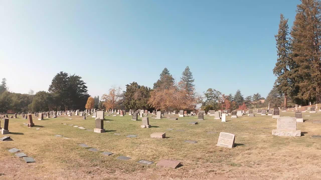 A slow pass across the path of graves and cemetery vase holders during the day.