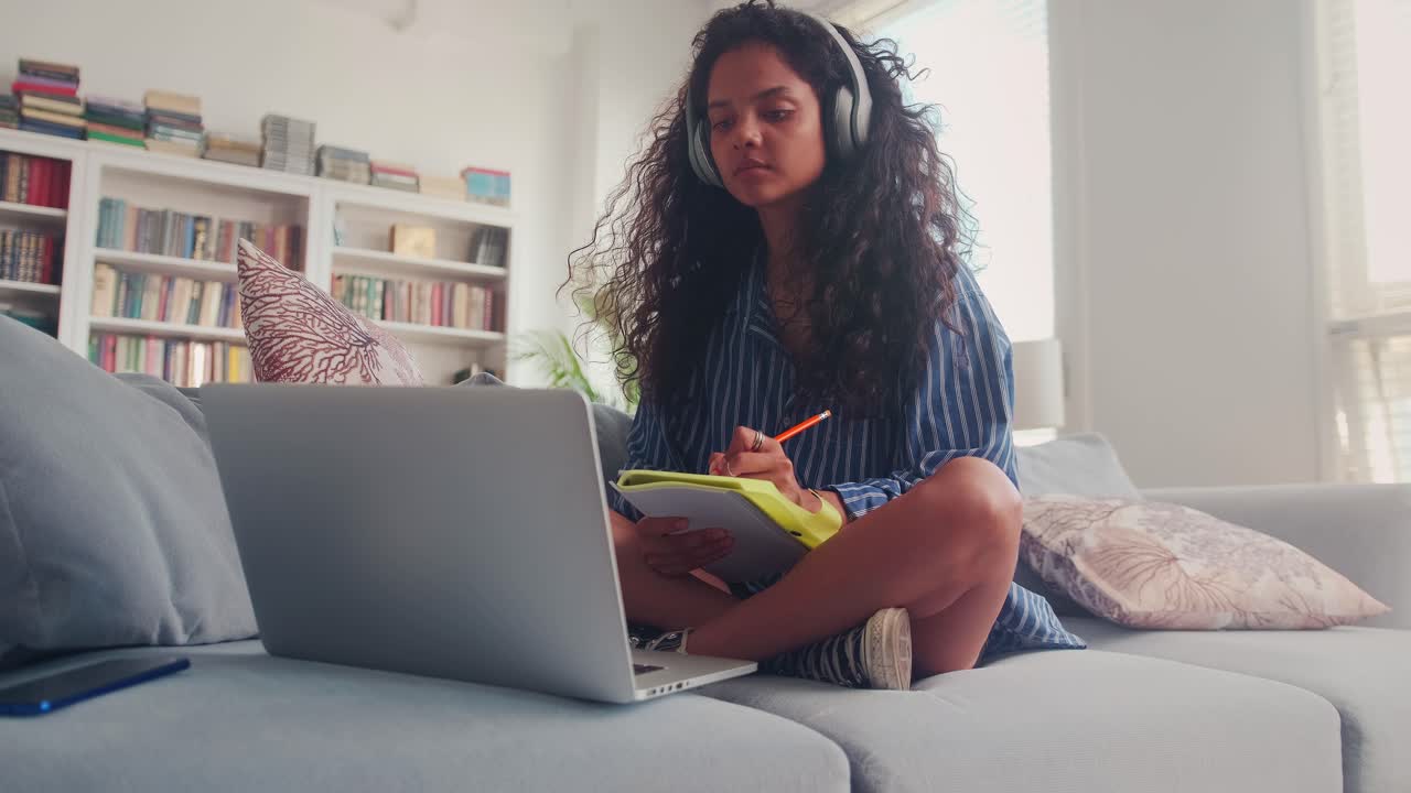 Focused indian teen girl making notes while listening to online lecture