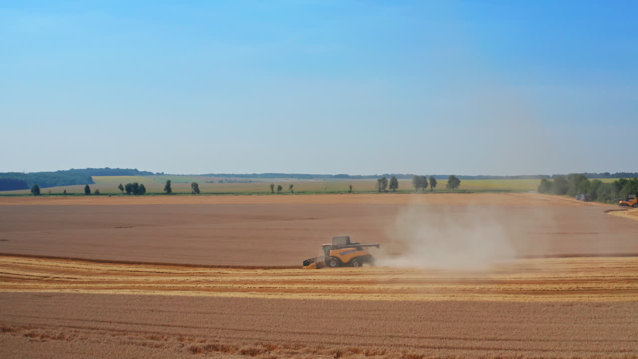 Beautiful countryside scenery with agribusiness plantations. Yellow harvester working in the field at foreground. Blue clear sky backdrop.