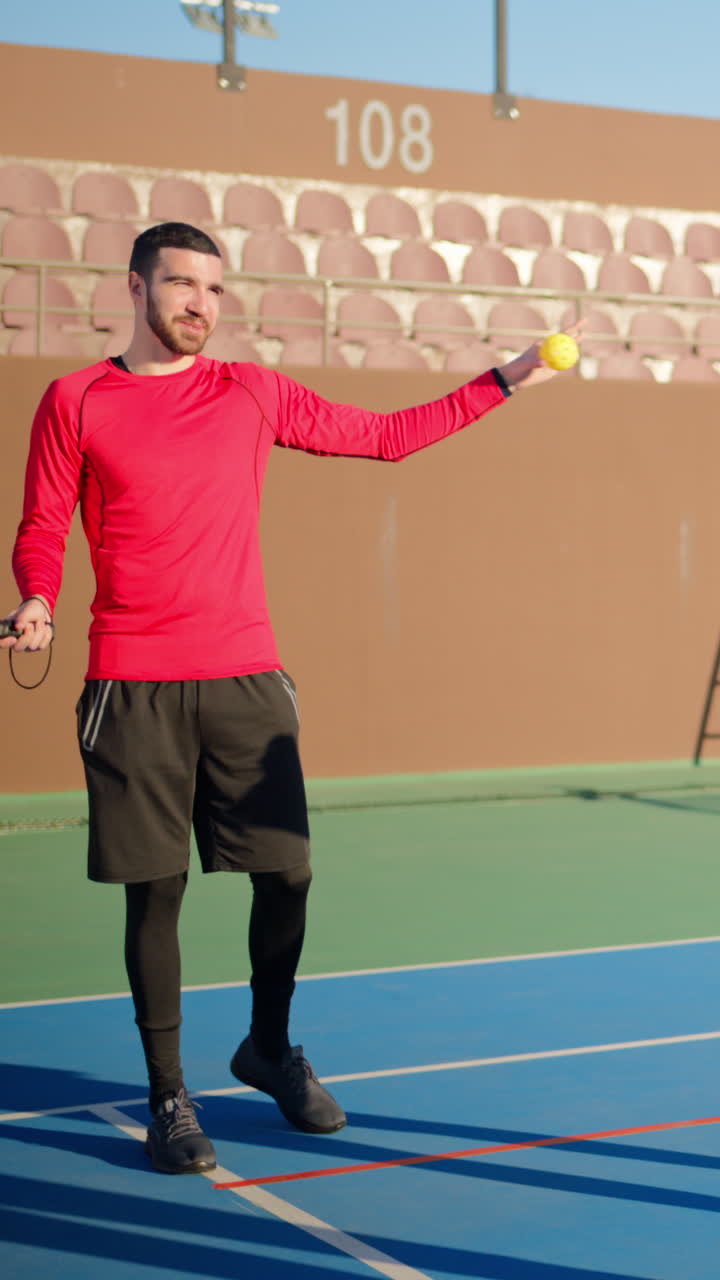 A man in a red shirt teaching how to play pickleball on a blue court on a sunny day. Vertical