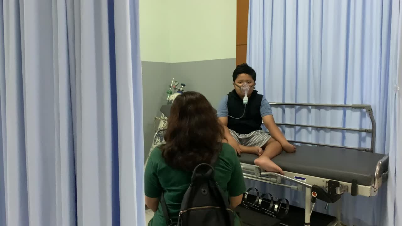 아시아 소년은 어머니와 함께 병원에서 네불라이저로 흡입을 합니다.