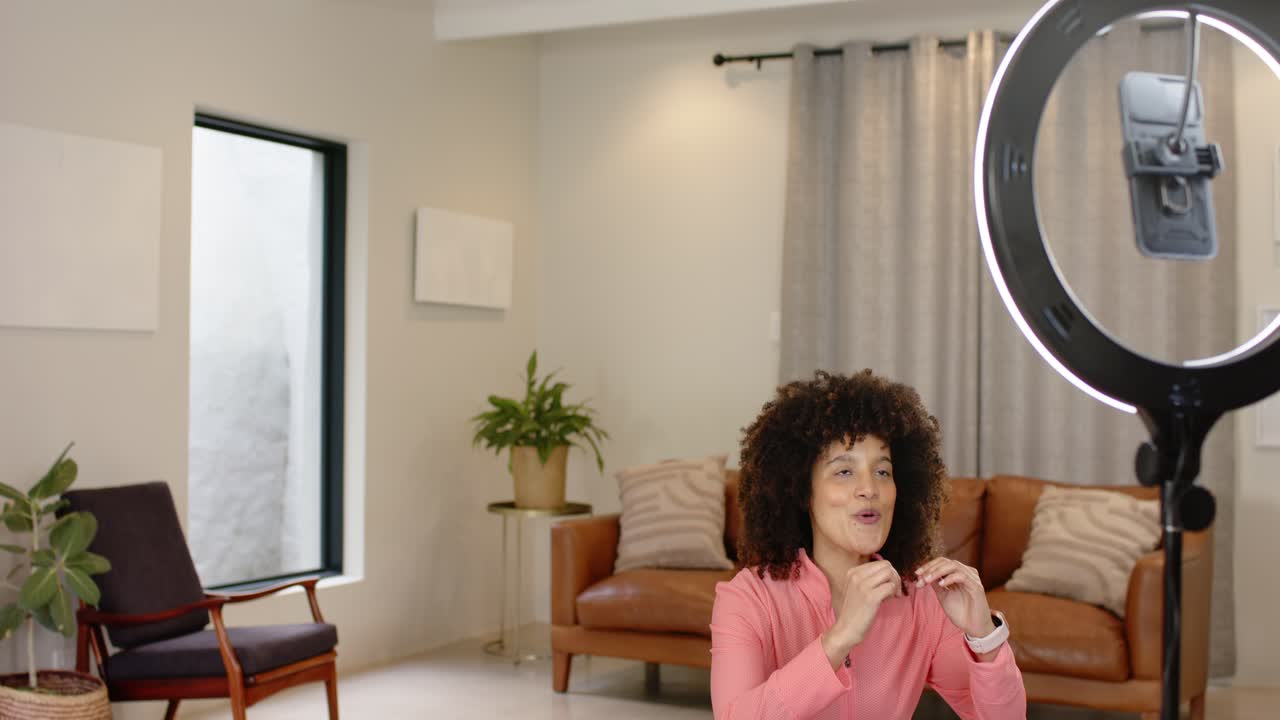 Donna che saluta una fotocamera con ring light a casa, riscalda le braccia e poi esegue squat per l'allenamento.